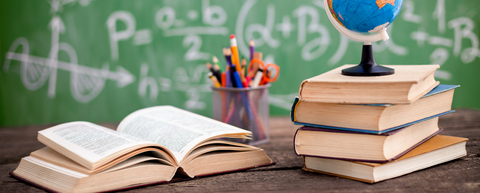 A globe on a stack of books and an open textbook on a desk, representing the Educator Legacy Award in front of a chalkboard.