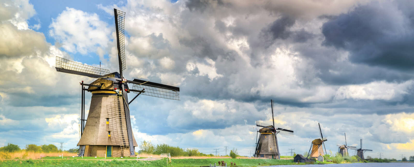 Historic windmills line a canal in the Netherlands under a dramatic sky, showcasing the iconic landscape of Holland.