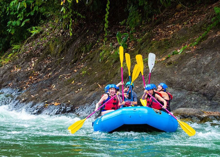 A group of people cheering while white water rafting on a river during an outdoor adventure in Costa Rica.