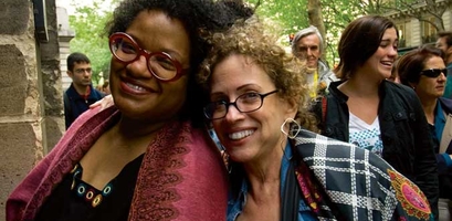 Two women smile for the camera in a crowd of people outdoors during a women-only event near a French canal.