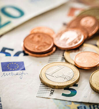 A close-up photograph of various euro coins and banknotes, including 50 and 20 euro bills, scattered together.