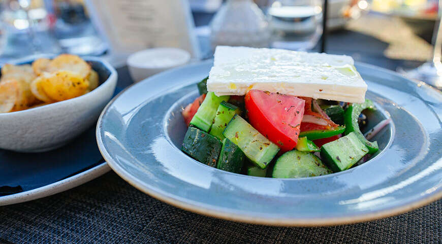 A traditional Greek salad with a large slice of feta cheese on top, served in a blue bowl in Greece.