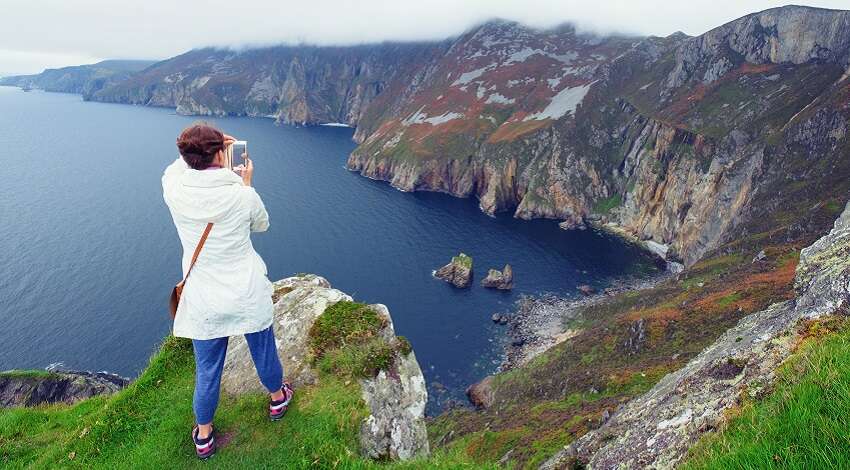 A woman takes a photo of the Slieve League sea cliffs