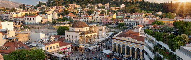 A scenic sunset view of Athens, Greece, showcasing the city's rooftops and the historic Acropolis perched on a hill under a beautiful sky.