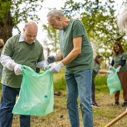 A group of volunteers in matching green shirts participate in a community clean up, a sustainable practice, by picking up trash in a park.