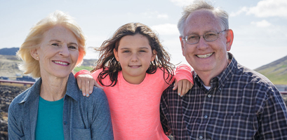 A smiling granddaughter stands between her grandparents in a rocky, outdoor setting, for a grandparent travel guide.