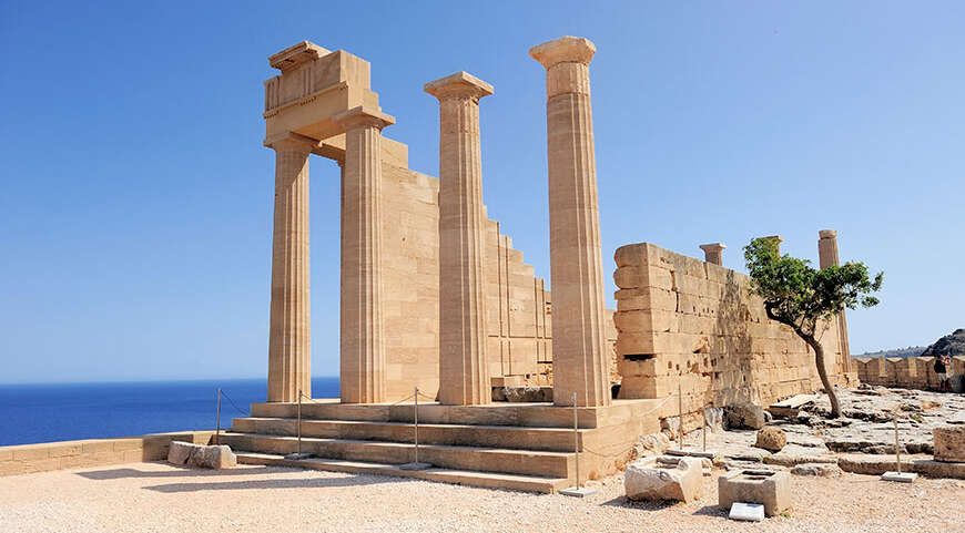 Sunlit stone ruins of an ancient temple with tall columns overlook the sea on the island of Rhodes, Greece.