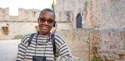 A smiling woman on a Road Scholar solo-only learning adventure in Rhodes, Greece, stands in front of ancient stone walls.