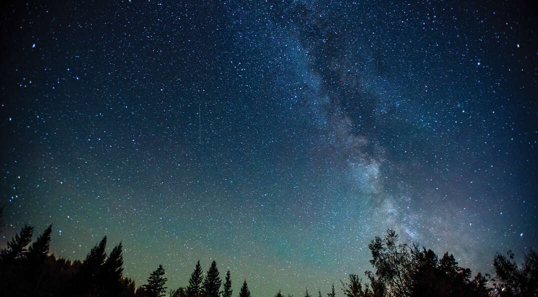 The Milky Way stretches across a star-filled night sky over Arizona forest silhouettes during the Grand Canyon Star Party.